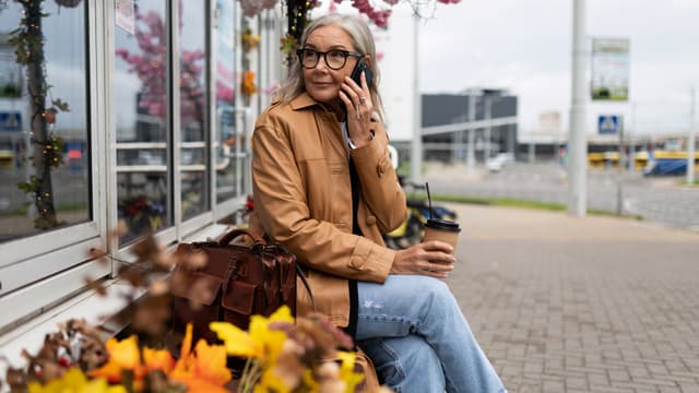 Nainen puhuu puhelimeen ja istuu penkillä