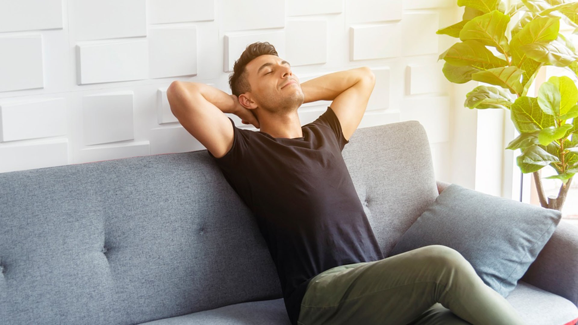 1920 Mies istuu harmaalla sohvalla ja nauttii kädet niskan takana raittiista sisäilmasta swegon