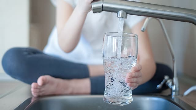 vettä hanasta juomalasiin pöydällä istuen