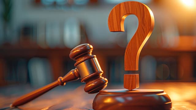 juristin nuija ja puinen kysymysmerkki pöydällä. taustalla kerrostalo