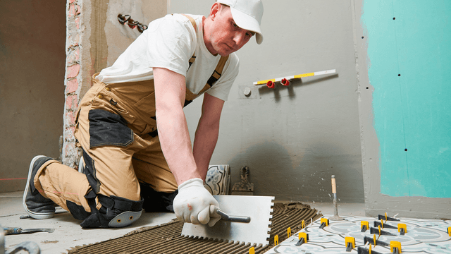 mies laatoittaa saunan lattiaa